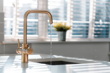 Elegant brushed gold dedicated water faucet steadily streams pure PFAS-free water filtered by an under-sink reverse osmosis purification system in bright kitchen.