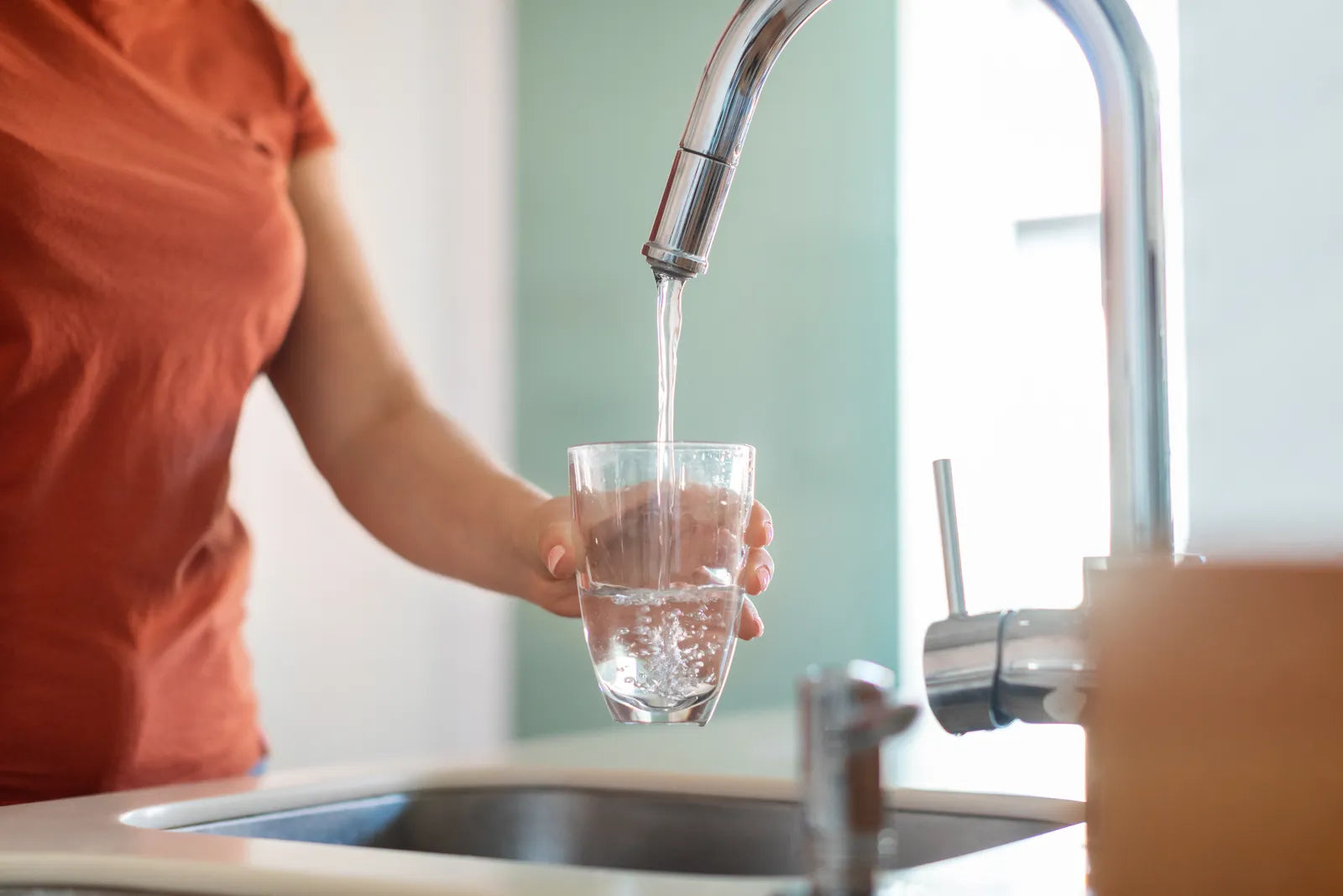 Clean tap water flowing into a clear glass in a modern kitchen, illustrating safe household drinking water, filtration awareness, and everyday hydration quality under US vs EU water standards comparison.