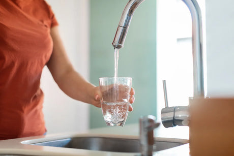 Clean tap water flowing into a clear glass in a modern kitchen, illustrating safe household drinking water, filtration awareness, and everyday hydration quality under US vs EU water standards comparison.