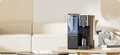 Frizzlife countertop water filtration system dispensing water into a glass on a table in a modern living room