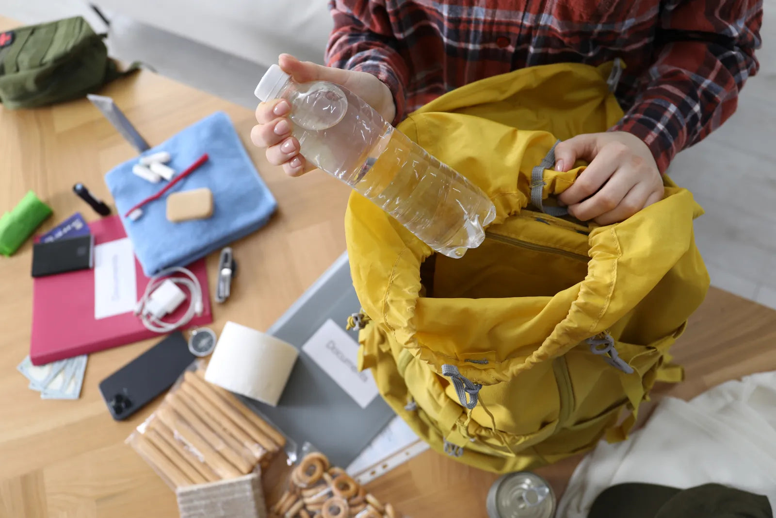 A traveler packs a water bottle into a backpack, preparing for safe hydration with a travel water filter.