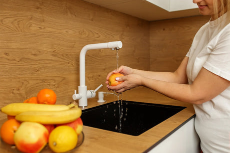 A woman rinses fresh fruits under a clean RO water tap in the kitchen.