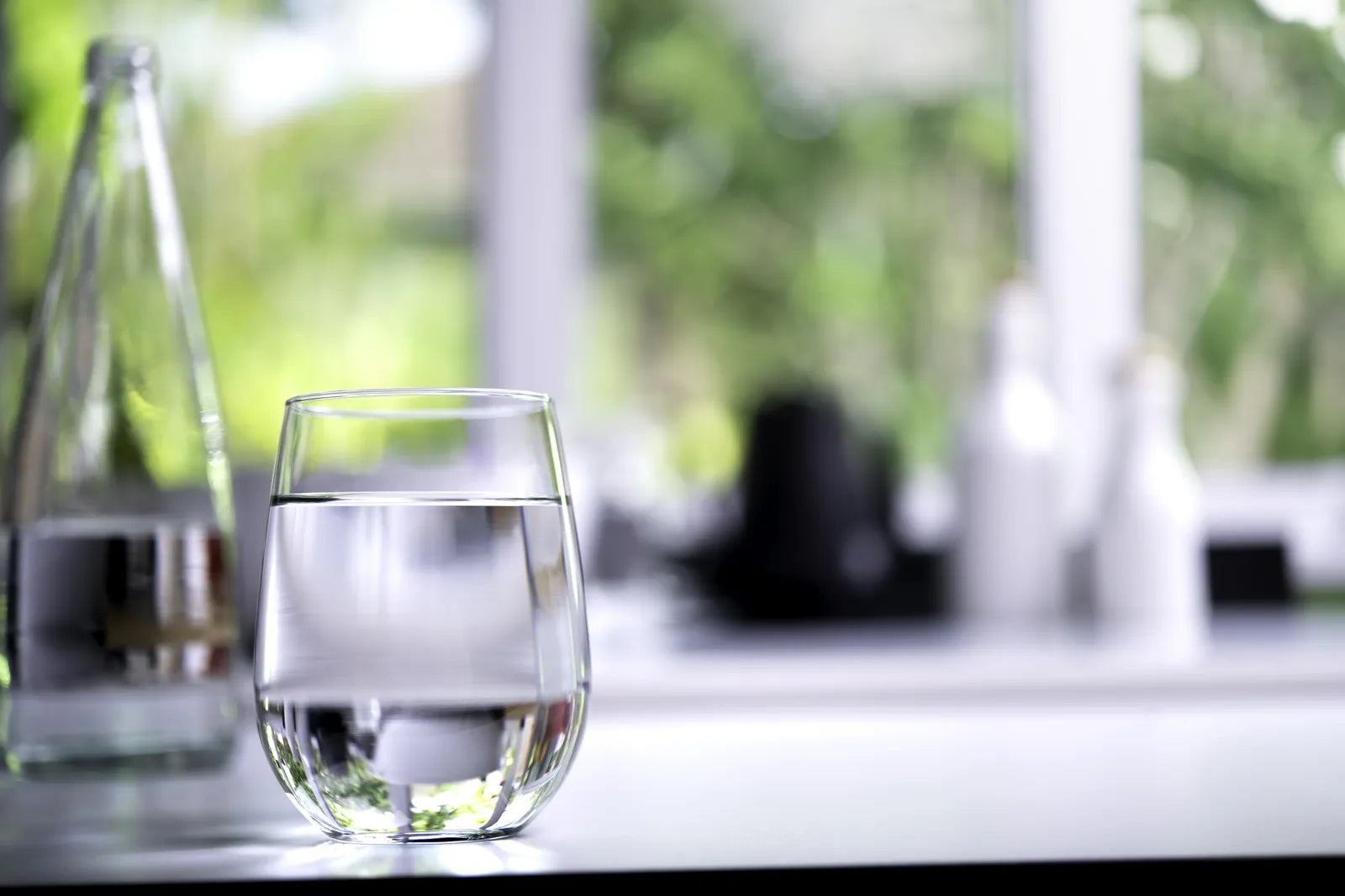 Clear glass of clean RO filtered drinking water placed by a sunlit window, illustrating fresh pure water output from both countertop and under-sink RO systems.