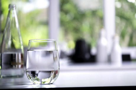 Clear glass of clean RO filtered drinking water placed by a sunlit window, illustrating fresh pure water output from both countertop and under-sink RO systems.