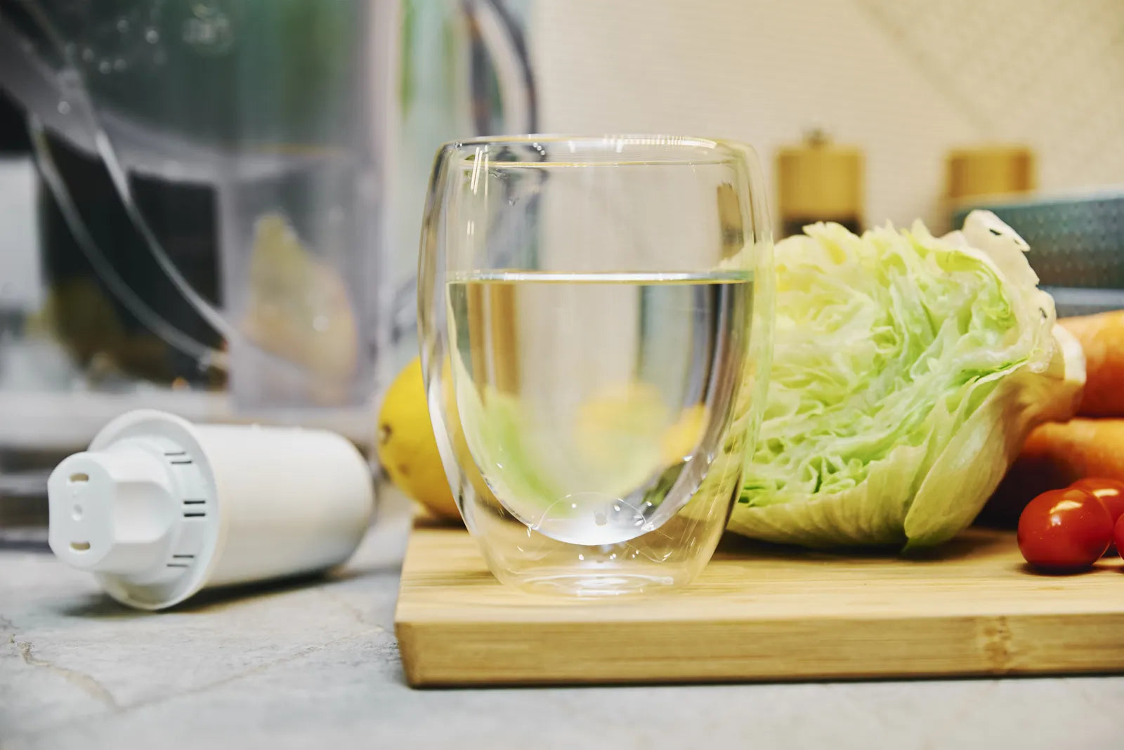 Glass of purified RO water on a kitchen counter with fresh vegetables and a water filter cartridge