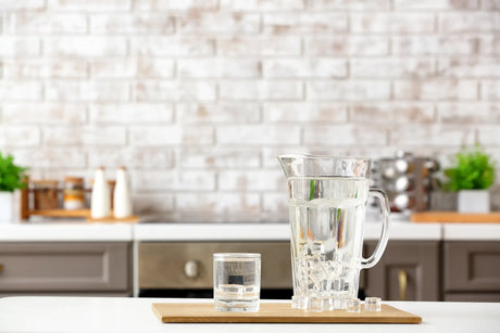 A glass pitcher of ice water and a glass sit on a kitchen counter, representing clean drinking water for home emergencies.