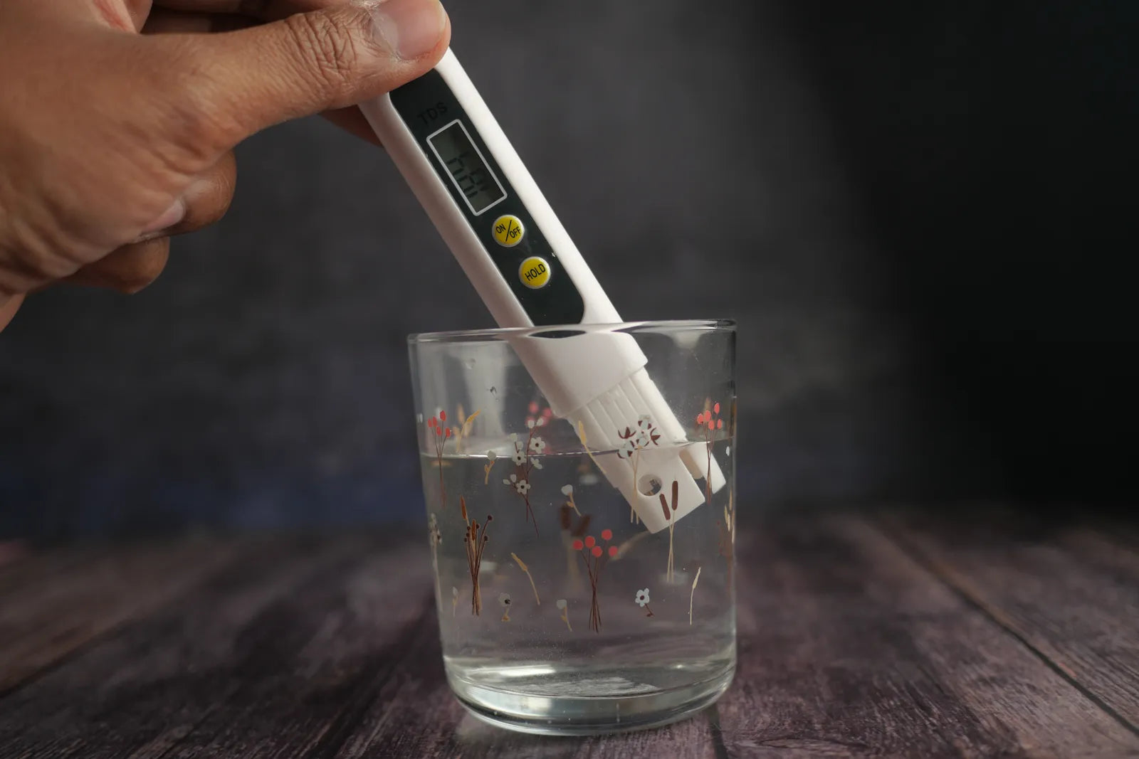 Hand holding a TDS meter to test water quality in a glass, used to measure feed and permeate TDS for RO rejection rate calculation