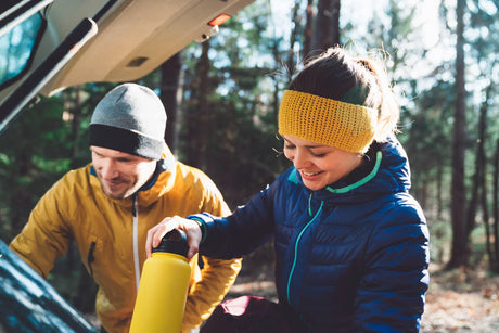 Two campers prepare a yellow water bottle, using a portable filter to remove fluoride from water during a forest trip.
