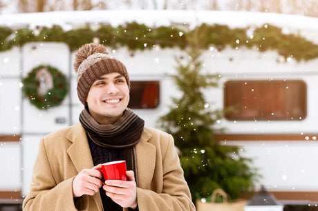 Man with a warm drink outside a snowy RV, illustrating the need to prep water filters before winter cold sets in.