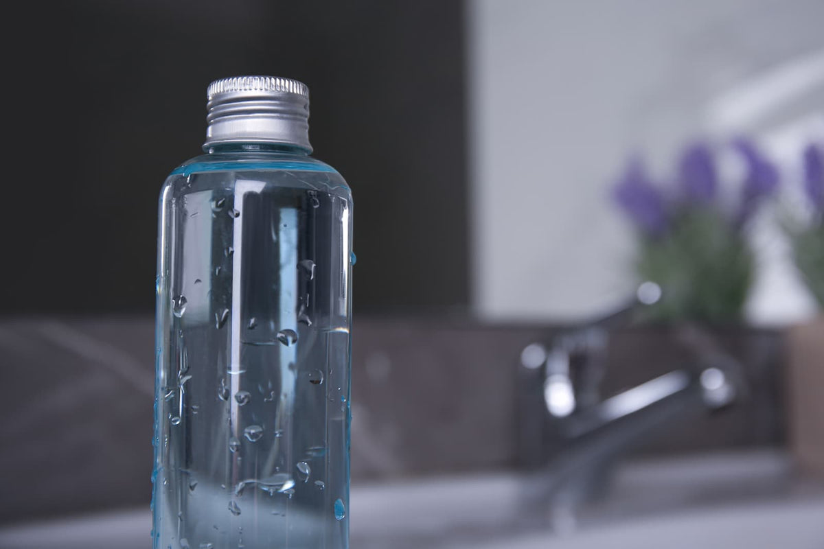 Factory-sealed drinking water and reusable bottle on a hotel counter near a sink.