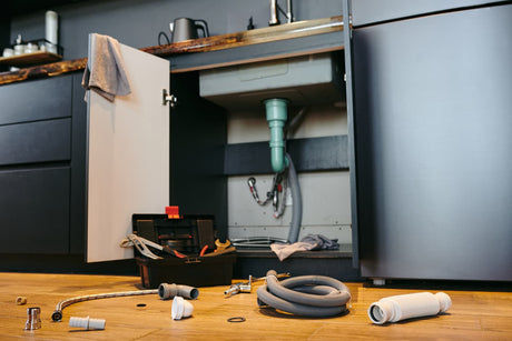 Open under-sink cabinet with exposed plumbing, hoses, fittings, and tools prepared for installation