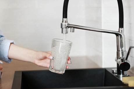 Hand filling glass from modern kitchen faucet, representing the importance of filtering tap water to remove pesticides and ensure purity.