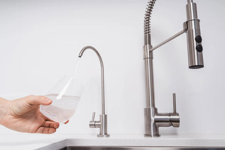 User fills a glass with fresh filtered water from a stainless steel reverse osmosis air gap faucet next to a regular kitchen mixer tap.