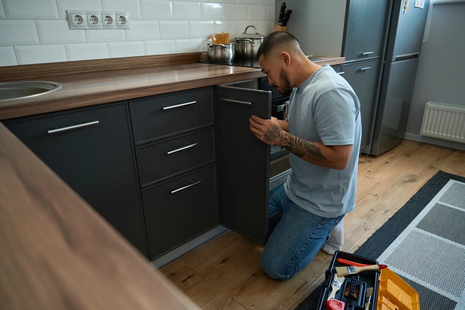 Man inspecting an under-sink cabinet while preparing plumbing for a refrigerator water connection.