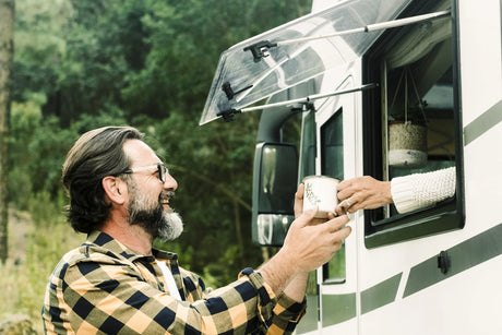Man receiving a coffee mug from an RV window, enjoying safe, filtered water while camping in nature