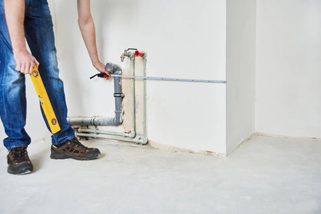 Worker measuring water pipe with level and tape measure for precise installation, ensuring proper alignment of plumbing lines.