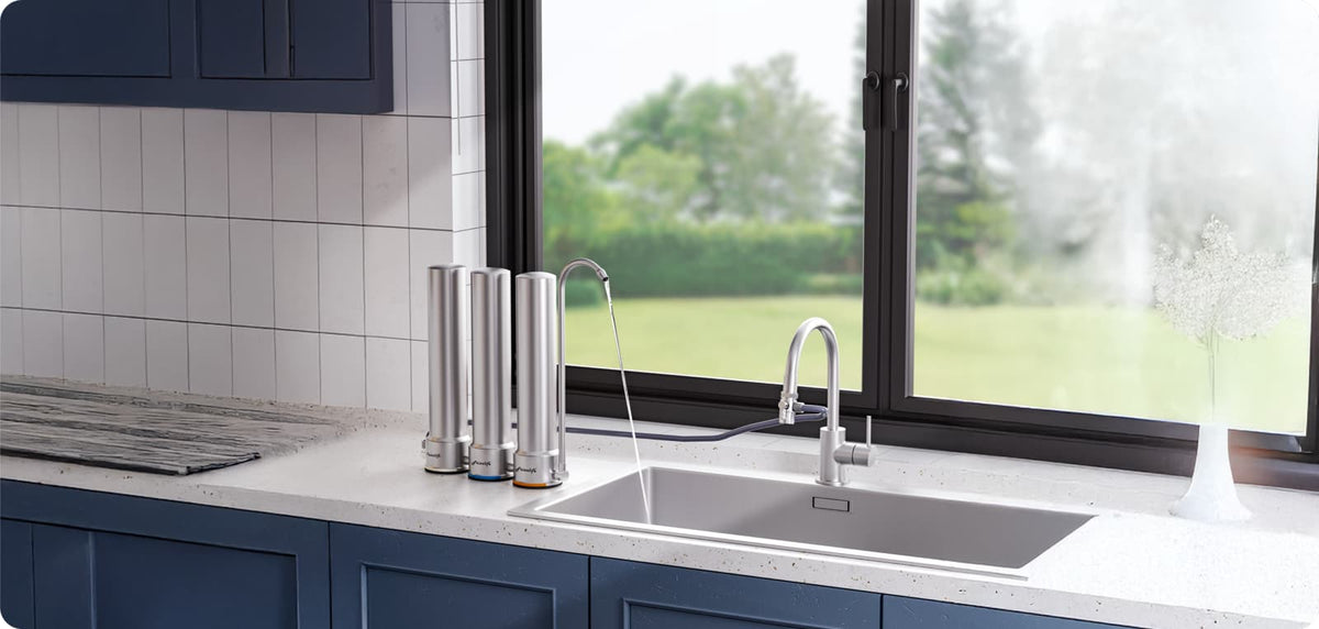 Three stainless steel water filter units installed beside a kitchen sink with a dedicated drinking water faucet