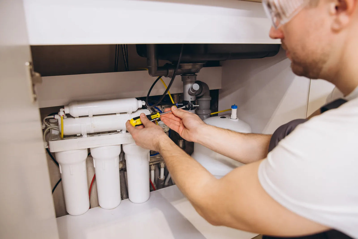 Technician uses a screwdriver to secure pipe connections on a traditional tanked under sink RO system, following official installation safety requirements.