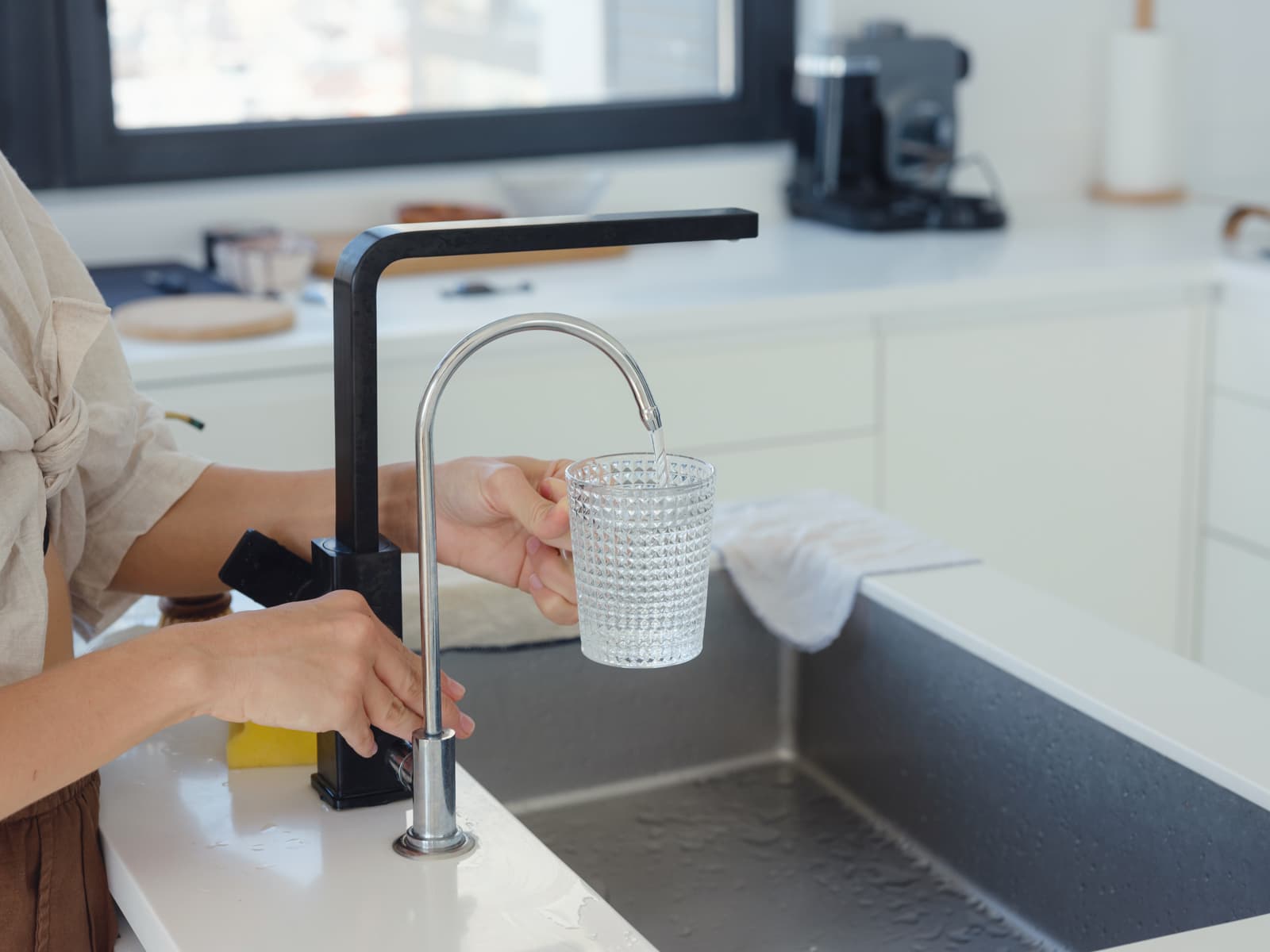 Filtered water flows from a dedicated drinking faucet into a glass beside the kitchen sink.