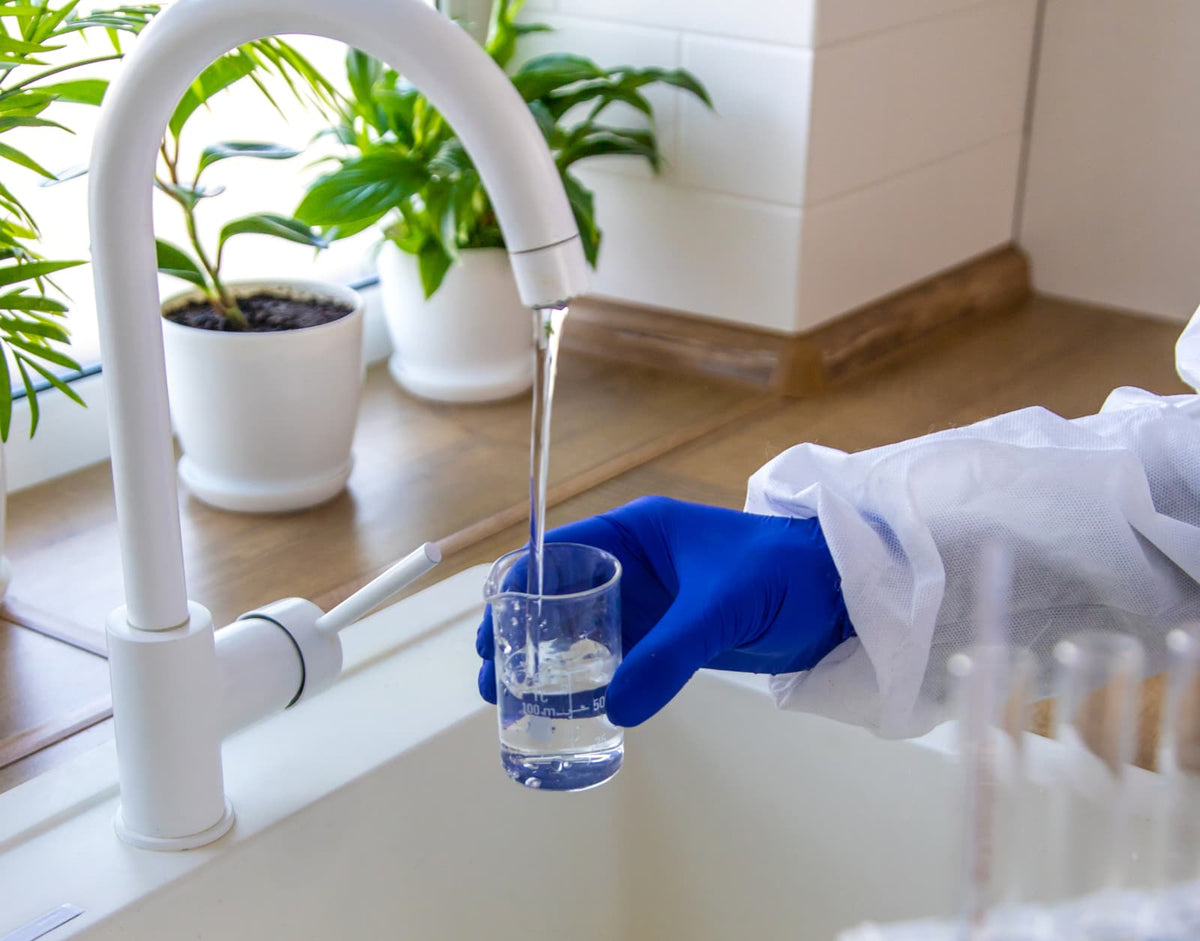 Gloved hand collecting tap water in a laboratory beaker for household water quality testing