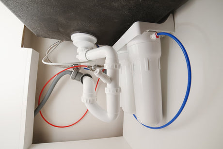 Under-sink water filter with red and blue tubing mounted beside the sink drain pipes.