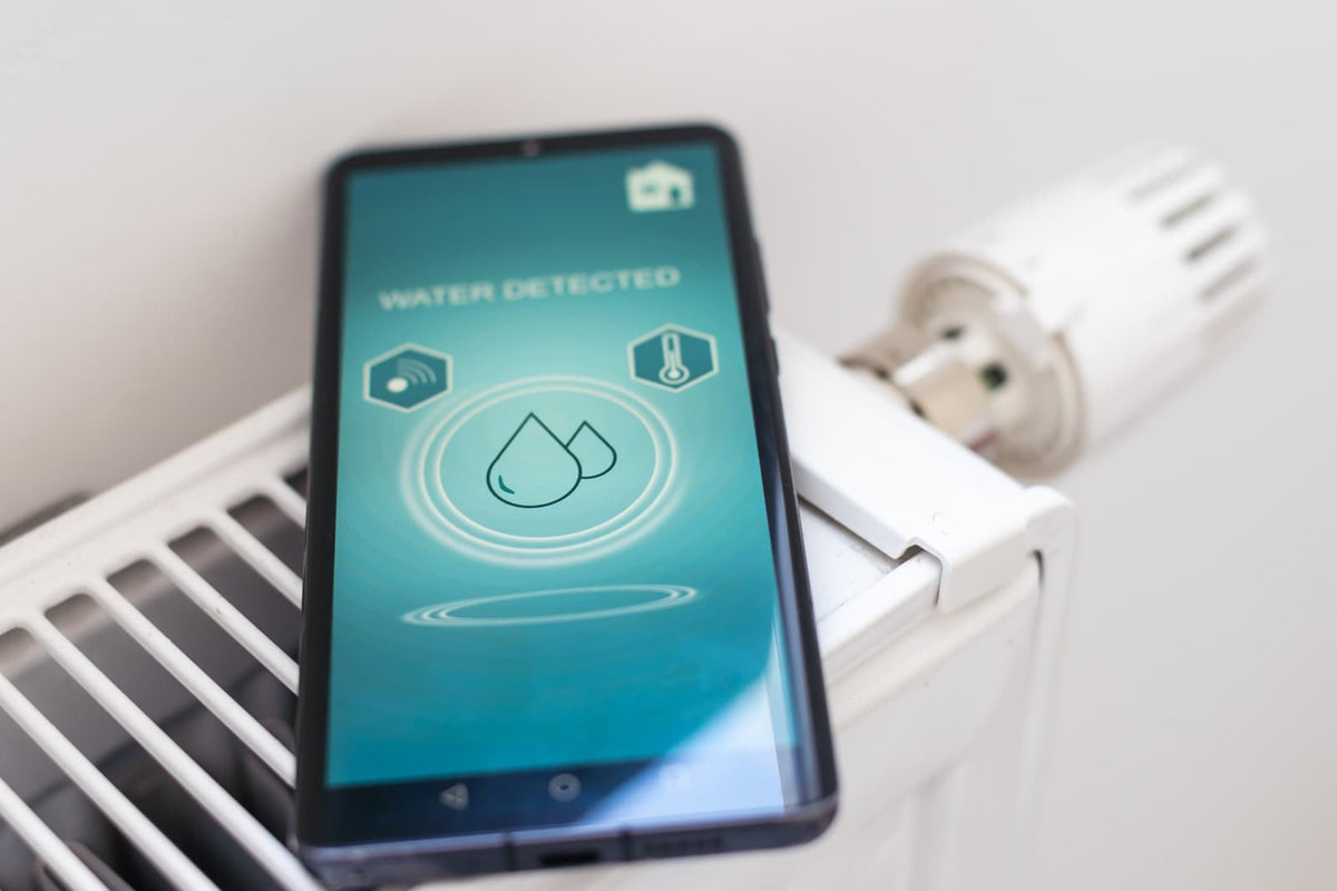 Smartphone displaying a water detection alert with water droplet icons beside a home radiator