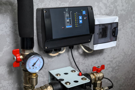 Wall-mounted water pressure monitoring control panel with a pressure gauge, valves, and connected plumbing pipes